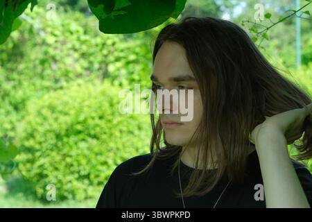 A young man stands thoughtfully amidst vibrant foliage, lost in reflection. Stock Photo