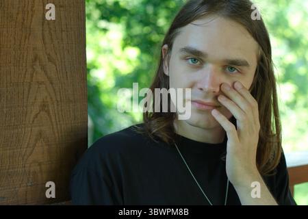 A young man gently touches his face while lost in thought outdoors. Stock Photo
