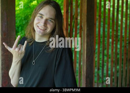 A young man smiles broadly while making a hand gesture in a vibrant green area. Stock Photo