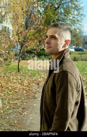 A thoughtful man stands in a park, appreciating the vibrant autumn colors around him. Stock Photo