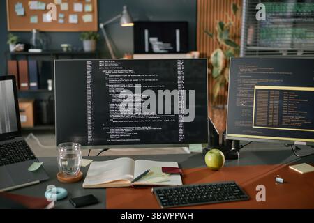 Computer monitor displaying programming code on desk with notebook, pen, glass of water, apple, and sticky notes, suggesting software development or coding workspace in modern office Stock Photo