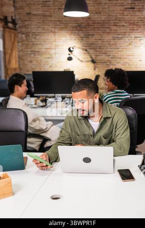 Focused employee working on laptop and smartphone in modern office Stock Photo