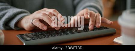 Website header shot of Caucasian middle aged man typing on wireless keyboard with both hands, wearing ring, focusing on work task, close up of hands and keyboard on desk Stock Photo