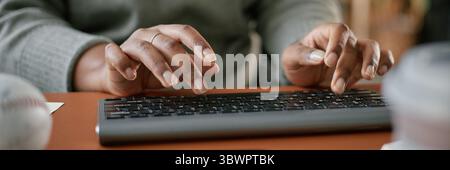 Website header shot of Black woman typing on wireless keyboard with both hands, close up of hands and fingers on keys, adult working at desk, focus on technology use and manual interaction Stock Photo
