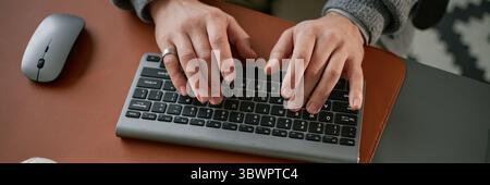 Website header shot of Caucasian middle aged man typing on wireless keyboard with both hands, wearing ring, working at desk with computer mouse nearby, close up of hands and keyboard Stock Photo