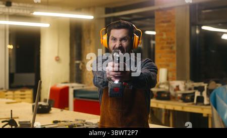 Expressive Caucasian handyman man wood master drilling electric instrument carpenter holding drill in workshop aggressive craftsman guy repairing male Stock Photo