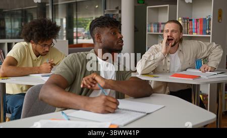 Three multiracial students studying learning in class lesson Caucasian guy asking question study problem talking showing ok diversity men guys writing Stock Photo