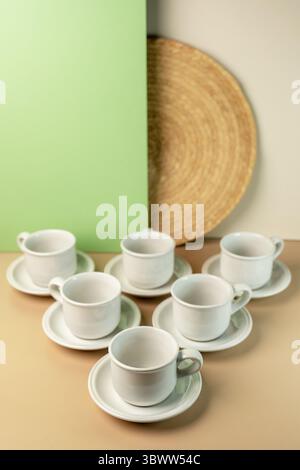 A set of clean, white ceramic coffee or tea cups and saucers arranged on a minimalist two-tone beige and green background with copy space. Stock Photo