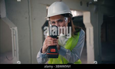 Caucasian woman worker builder looking at camera view of rotary drill repair strong power female girl engineer contractor in helmet vest safety Stock Photo