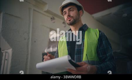 Serious Caucasian male engineer mechanic builder man writing tablet foreman guy planning draft structure in factory workshop architect drawing Stock Photo