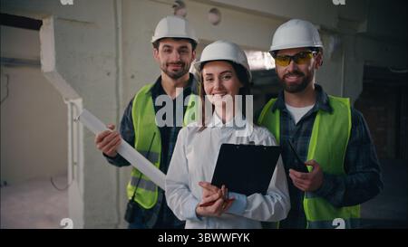 Happy three Caucasian foremen workers males guys architects men looking at camera female portrait team handymen mechanics woman cooperation in Stock Photo