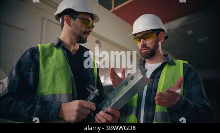 Caucasian men guys builders engineers talking discussing work repair in construction manufactory contractors repairmen holding metal detail Stock Photo