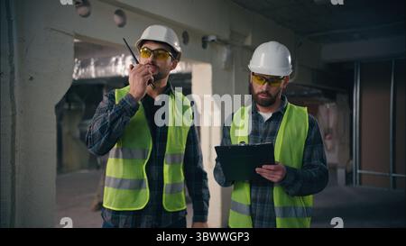 Two Caucasian foremen guys builders control industrial work in construction technicians men architects building cooperation handymen in safety uniform Stock Photo