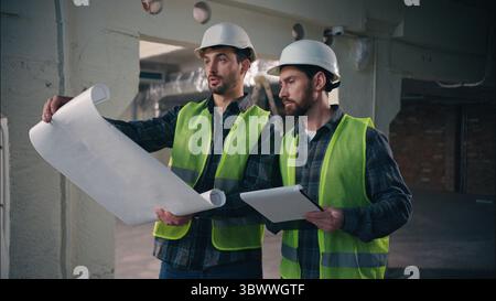 Professional Caucasian guys conversation holding paper blueprint in construction cooperation builders men engineers electricians draft technicians Stock Photo