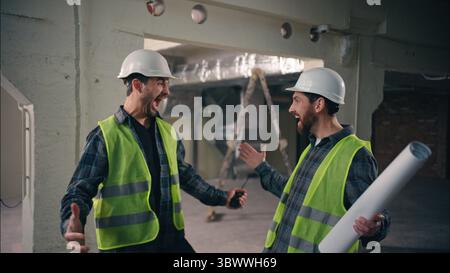 Two happy Caucasian men greeting friends buddies males guys workers in uniform helmets business construction teamwork engineers architects meeting Stock Photo