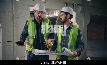 Two contractors civil engineers discuss arguing Caucasian men builders males conflict problem architects workers talking blueprint paper disagreement Stock Photo
