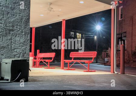 Red benches under awning on side of building at night. Stock Photo