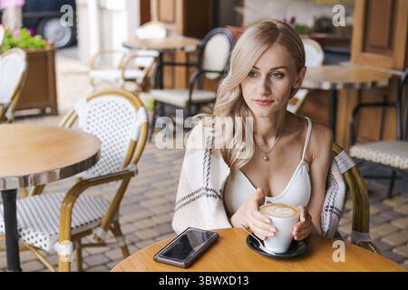 Young woman relaxing in cafe at table on the street, happy caucasian woman Stock Photo