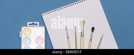 A set of brushes, a sketchbook, and bright watercolours on a blue background. the concept of creativity Stock Photo