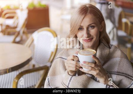 Young beautiful happy woman with long curly hair enjoying a cappuccino on the street Stock Photo