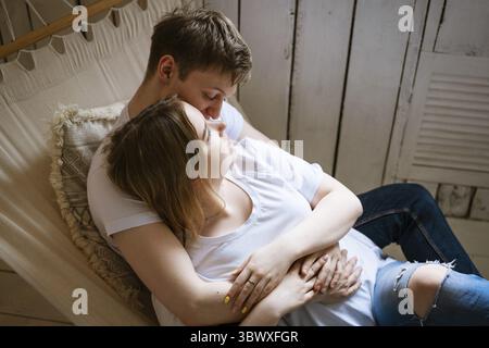 Portrait of a young beautiful couple, a young adult man and a woman in a hammock. the woman is an attractive blonde, the man is dark-haired in a white Stock Photo
