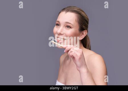Smiling caucasian female adult using eco-friendly bamboo toothbrush with charcoal toothpaste. Stock Photo