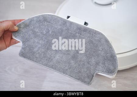 Hand holding robotic vacuum mop attachment for efficient home cleaning on light wooden floor. Stock Photo