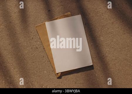 Blank paper greeting card, invitation. Craft envelope, textured concrete stone background. Natural sunlight, shadows. Minimal composition. Wedding Stock Photo