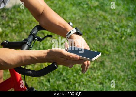 Cyclist standing and checking fitness progress in apps after riding with smartphone. Summer activity. Close up Stock Photo