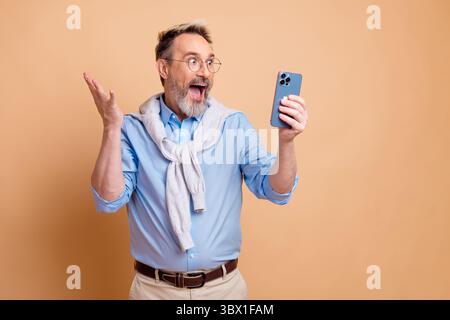 Portrait of a cheerful mature businessman holding smartphone in one hand and making welcoming gesture against beige background Stock Photo