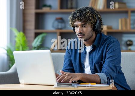 A young man with headphones working on a laptop from home, attending a virtual meeting or studying remotely. Stock Photo