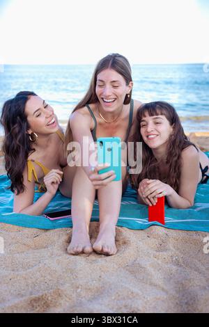 Vertical portrait three young woman using smartphone app on the beach Stock Photo