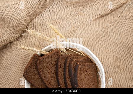 Top‑view of a white wicker basket holding several slices of dark rye bread and golden wheat stalks, set on a rustic burlap fabric for a natural, artis Stock Photo