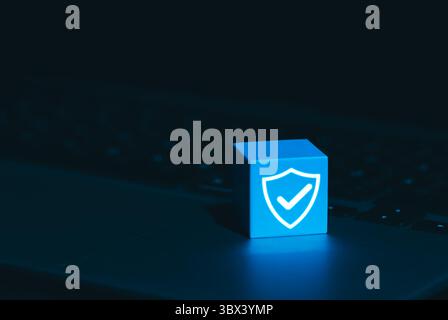 Cybersecurity and Data Protection Symbol Concept. A glowing blue cube with shield and checkmark icon on laptop keyboard, symbolizing cyber security, Stock Photo