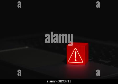 Cybersecurity Warning Alert Symbol. Glowing red warning triangle block with exclamation mark placed on laptop, symbolizing system threat or cyber Stock Photo