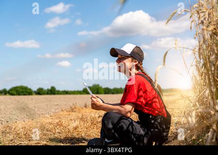 Female agricultural worker using digital tablet while sitting on farmland near field Stock Photo