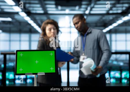 Green screen laptop used by system administrators in data center inspecting supercomputers, updating network topologies. Close up of mockup notebook next to man and woman in server farm Stock Photo