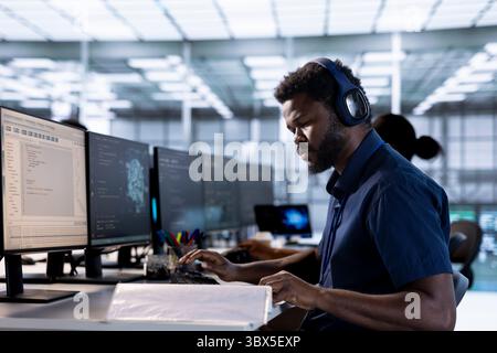Server room programmer listening music, looking over paperwork after creating high performance AI systems on PC. Engineer in data center wearing headphones checking artificial intelligence documents Stock Photo