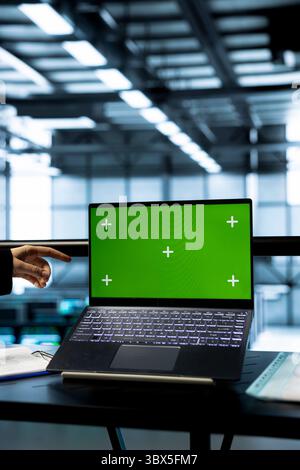 Technicians in data center using green screen mockup laptop, inspecting server clusters, updating network topologies. IT experts using chroma key notebook, ensuring stable operations Stock Photo