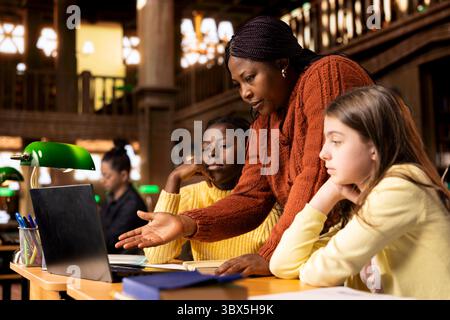Female teacher assisting pupils with class homework and mentoring them, providing academic instruction and support to help them pass their school assignments. Tutor lecturer gives private lessons. Stock Photo