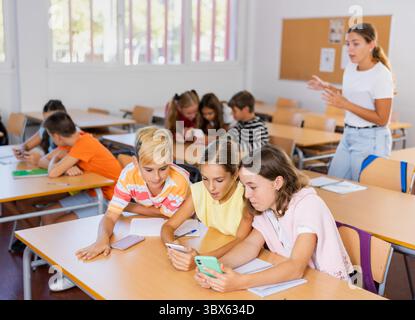 Modern curious preteen schoolchildren using smartphones at lesson Stock Photo