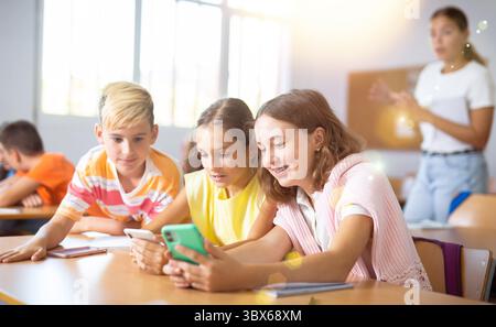 Interested preteen schoolchildren using phones during lesson in classroom Stock Photo