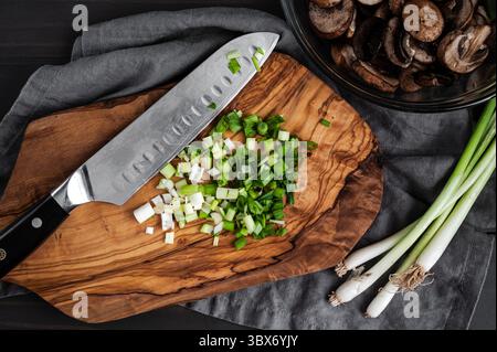 Sliced Scallions on a Wooden Cutting Board: Sliced green onions on a chopping board with a santoku knife and sliced cremini mushrooms on the side Stock Photo