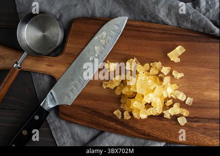 Diced Candied Pineapple on a Wooden Cutting Board: Chopped pieces of candied pineapple on a wood carving board with a santoku knife and measuring cup Stock Photo
