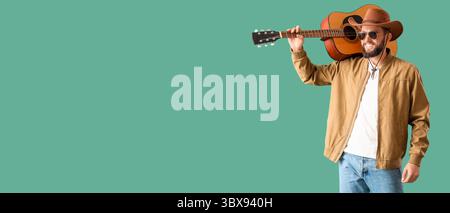 Handsome young man in stylish cowboy hat holding guitar on green background with space for text Stock Photo