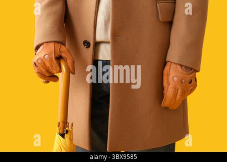 Man in stylish brown leather gloves with umbrella on yellow background, closeup Stock Photo