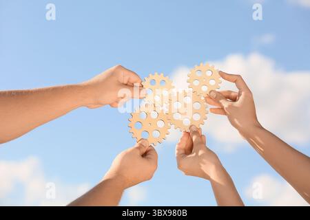Hands with wooden gears against sky Stock Photo