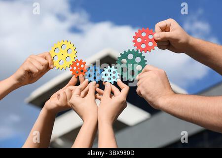 Many hands with colorful gears outdoors Stock Photo