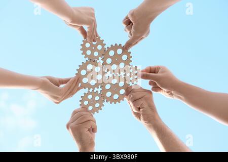 Many hands with wooden gears against sky, bottom view Stock Photo