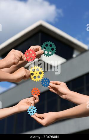 Many hands with colorful gears outdoors Stock Photo